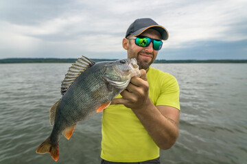 Successful perch fishing. Happy fisherman hold big perch fish on lake background