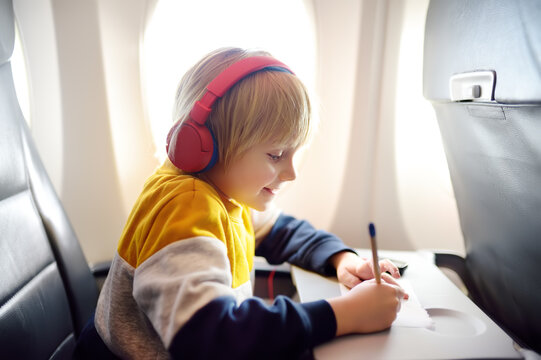 Cute little boy traveling by an airplane. Child using player to listen a music or audiobook during the flight and drawing pictures. Entertainment for kids on a board of plane