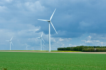 Rural landscape in France with blue sky and green field with spinning wind power stations producing environmentally friendly electric energy.