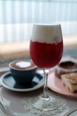 Red drink in a wine glass and coffee in the background