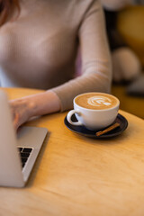 cropped view of young woman using laptop near cup of cappuccino.