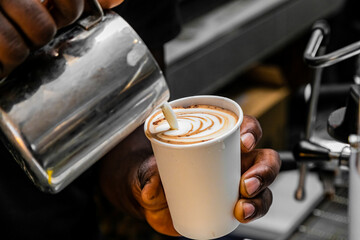 African Coffee Barista pouring a heart shape with milk foam.