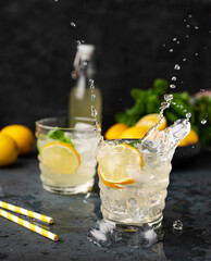 Two glasses of Lemonade drink with fresh lemon and splashes. Refreshing cocktails with lemons, mint...