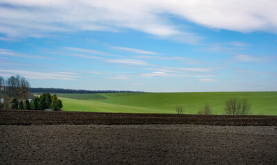 panoramic view of plowed field with green field, blue skies wiith clouds, agriculture in spring