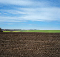 plowed field with blue skies and clouds, agriculture in spring