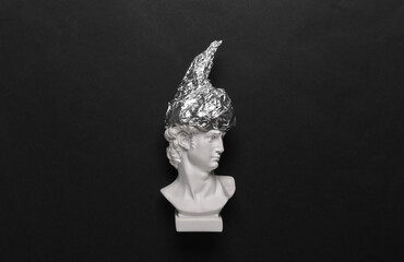 Antique david bust in foil hat on a black background. Conspiracy theory - obrazy, fototapety, plakaty