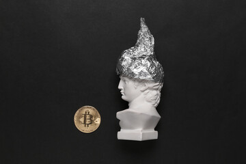 Antique david bust in foil hat and bitcoin on black background. Conspiracy theory