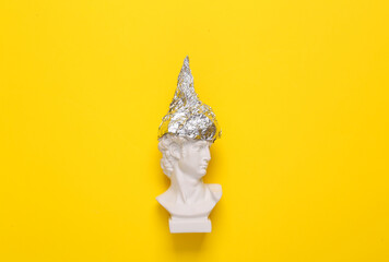 Antique david bust in foil hat on yellow background. Conspiracy theory - obrazy, fototapety, plakaty