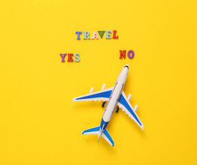 Travel yes or no. Miniature airplane on a yellow background. Travel concept, flat lay
