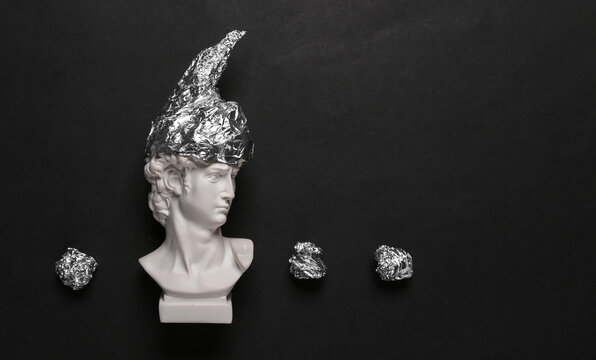 Antique David Statue In Foil Hat On Black Background. Conspiracy Theory