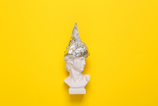 Antique david bust in foil hat on yellow background. Conspiracy theory