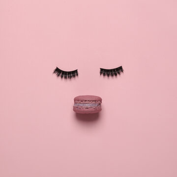 Conceptual pop minimal still life. Face shape from false eyelashes and macaroons on a pink background. Flat lay