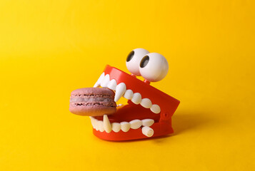 Toy jaw vampire with french macaroon in the teeth on yellow background. Halloween concept