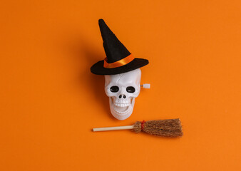 Obraz premium Minimal halloween still life. Skull in a witch's hat with a broom on orange background. Top view