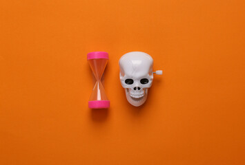 Clockwork skeleton skull toy with hourglass on orange background. Minimal halloween layout. Top...