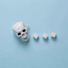 Skeleton skull with sugar cubes on a blue background. The concept of the harm of sugar to life,...