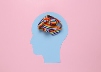 Paper cut human head with lgbt rainbow ribbon in place of brain on pink background