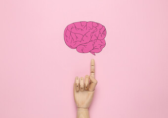 Paper brain with the finger of a wooden hand pointing at it on a pink background. The concept of...