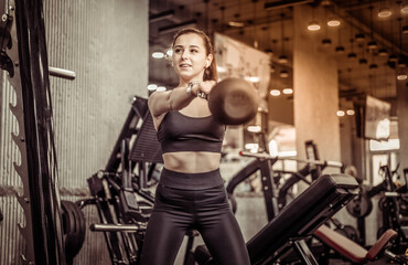 Fototapeta na wymiar Young athletic woman working out with a kettlebell in her hands, doing swings in the gym
