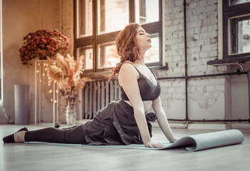 Young brunette woman in sportswear practices yoga asana on the mat in yoga studio. Cobra pose