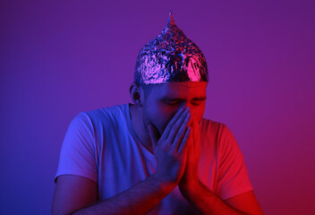 A bearded man in a foil hat coughs in the red-blue neon light. Conspiracy. Conspiracy theory - obrazy, fototapety, plakaty