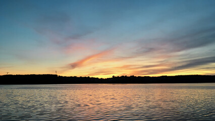 Beautiful sunset over lake Natural background with blue water and sky with yellow orange purple clouds, reflected in the lake. Breathtaking horizon panoramic view with setting sun.