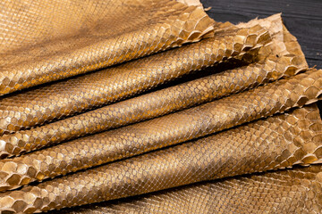golden brown metallic dyed folded natural genuine python leather on the wooden table	