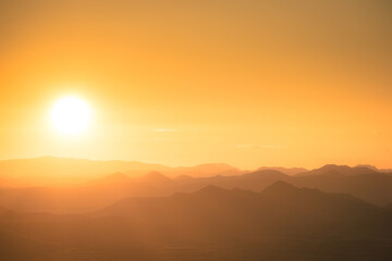 The sun setting behind the mountains of the Sonoran Desert in Arizona with the air lit up in golden light with mountains in silhouette.