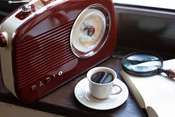 A cup of black coffee, a book and a retro-style radio are located on a wooden windowsill. Theme of English breakfast.