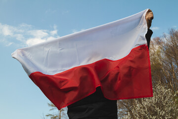 Woman holding flag of Poland against blue sky. 3 May Polish Constitution Day (3rd May National...