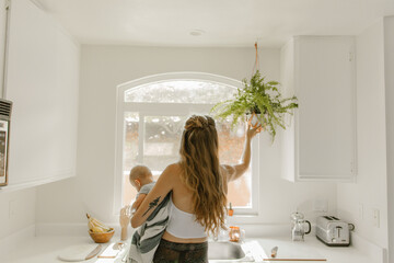 mother and baby in kitchen watering hanging plant