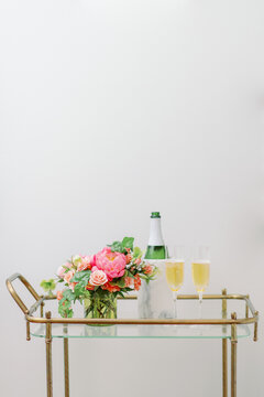 pink and peach flowers on bar cart with champagne and two glasses