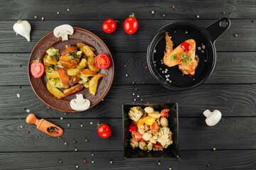 Fried potatoes with mushrooms and tomatoes on a black wooden bac