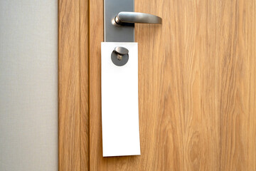 Paper blank label as mockup on door handle at the hotel. Wooden pine door and white long sheet with...