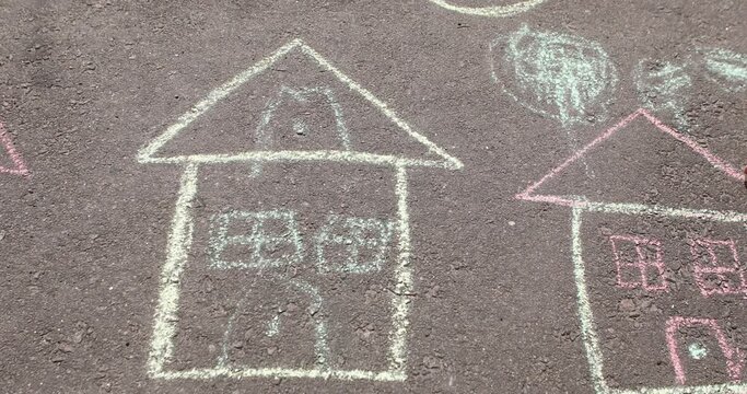 a little girl draws a house with chalk on the pavement.