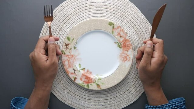 hand holding cutlery with empty plate on wooden table 