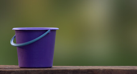 Purple bucket stands on wooden boards. Pot in the garden on a blurred green background.