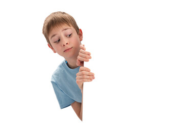 Schoolboy cautiously peeks out from behind board with empty space. Boy looks out from behind banner. Copy space.