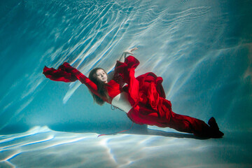 Attractive red-haired young woman swims beautifully underwater in a red dress