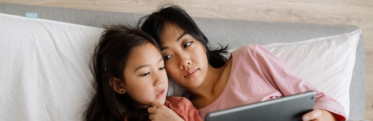 Asian mother and daughter using laptop while sitting on bed