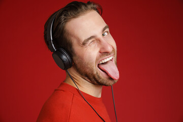 Young bristle man in headphones winking while showing his tongue