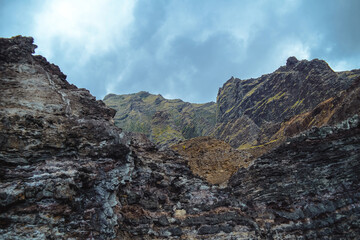 The gorgeous rugged wilderness and cliffs of Kauai's Napali Coast in Hawaii, with low clouds and mist hanging over the mountain peaks under a stormy grey sky