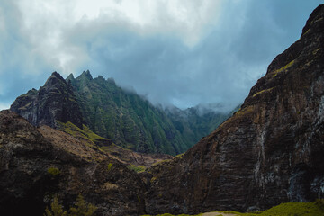 The gorgeous rugged wilderness and cliffs of Kauai's Napali Coast in Hawaii, with low clouds and mist hanging over the mountain peaks under a stormy grey sky