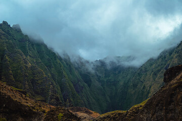 The gorgeous rugged wilderness and cliffs of Kauai's Napali Coast in Hawaii, with low clouds and mist hanging over the mountain peaks under a stormy grey sky