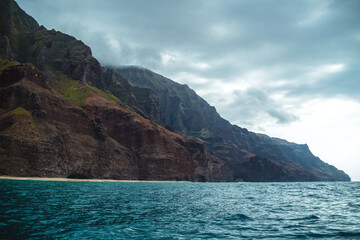 Fototapeta na wymiar The gorgeous rugged wilderness and cliffs of Kauai's Napali Coast in Hawaii, with low clouds and mist hanging over the mountain peaks under a stormy grey sky, and bright blue and teal ocean waves