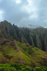 The gorgeous rugged wilderness and cliffs of Kauai's Napali Coast in Hawaii, with low clouds and mist hanging over the mountain peaks under a stormy grey sky © Kaitlin