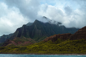 The gorgeous rugged wilderness and cliffs of Kauai's Napali Coast in Hawaii, with low clouds and mist hanging over the mountain peaks under a stormy grey sky