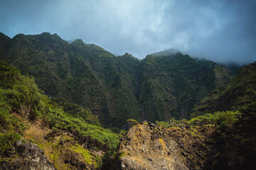 The gorgeous rugged wilderness and cliffs of Kauai's Napali Coast in Hawaii, with low clouds and mist hanging over the mountain peaks under a stormy grey sky