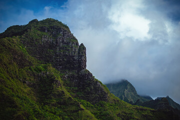 The gorgeous rugged wilderness and cliffs of Kauai's Napali Coast in Hawaii, with low clouds and mist hanging over the mountain peaks under a stormy grey sky