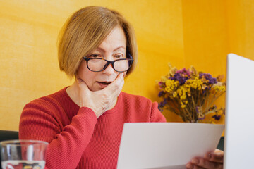 Shocked worried mature woman reading paper document or postal letter feeling frustrated by...